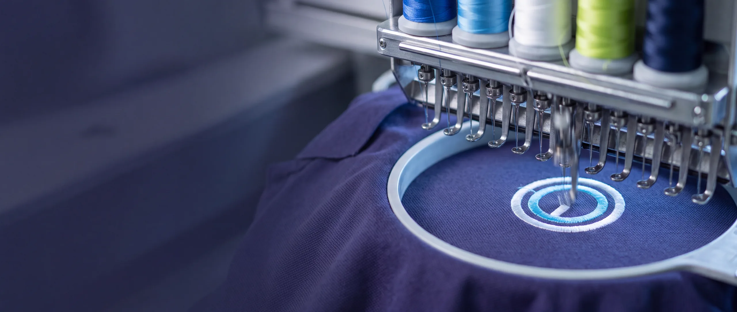 Industrielle 15-Nadel-Stickmaschine stickt ein Firmenlogo auf ein dunkelblaues Poloshirt